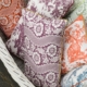 Le coussin décoratif XCOMM_COUSSIN 30X50 FLEURS AMARANTE, aux motifs floraux complexes, est disposé dans un panier tressé blanc. la marque Toile de Jouy