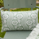 Le XCOMM_COUSSIN 30X50 FLEURS SAUGE, un coussin rectangulaire avec un motif floral vert et blanc, est posé sur une chaise en métal vert clair à l'extérieur, entourée d'herbe. la marque Toile de Jouy