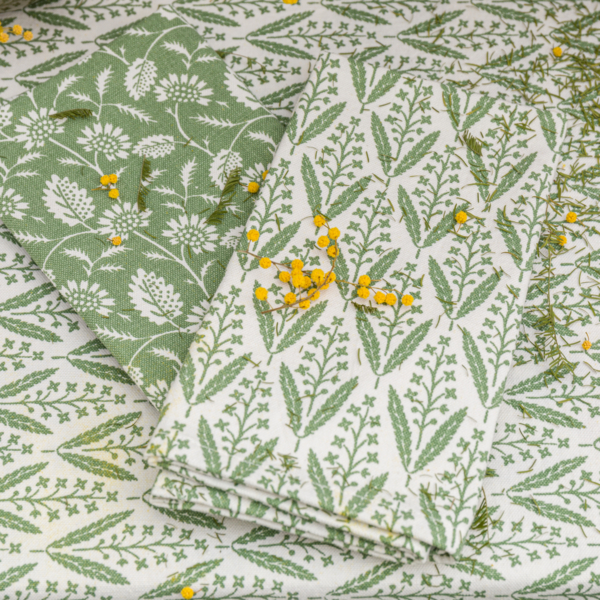 Deux serviettes XCOMM_SERVIETTES/ 6 CHARDON SAUGE aux imprimés botaniques verts reposent sur une surface assortie, ornée de fleurs et de feuillages jaunes pour ajouter de la couleur et de la texture. la marque Toile de Jouy
