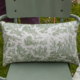 Le XCOMM_COUSSIN 30X50 FLEURS SAUGE est un coussin rectangulaire représentant des scènes de campagne en toile verte sur tissu blanc, en extérieur sur une chaise en métal vert clair sur fond d'herbe. la marque Toile de Jouy