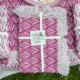Le XCOMM_SET DE TABLE/2 EPIS AMARANTE présente des nappes à motifs violets et blancs pliées avec des bords à franges, nouées avec un ruban blanc et étiquetées, présentées sur un fond de tissu assorti. la marque Toile de Jouy