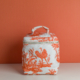 Le modèle XCOMM_TROUSSE POULETTE4 PARTIES MANDARINE est un sac en tissu blanc orné d'un motif « toile » orange représentant des personnages et des animaux, muni d'une poignée sur le dessus et d'une fermeture à glissière, présenté sur une surface blanche avec un fond orange. la marque Toile de Jouy
