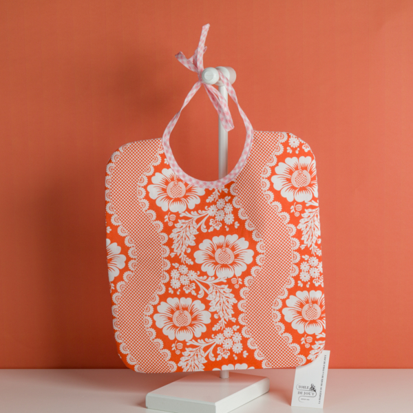 Une pochette « XCOMM_TROUSSE STYLOS OFFRANDE SAUGE » est présentée sur un présentoir blanc devant un fond orange, avec une petite carte pliée posée à proximité. la marque Toile de Jouy