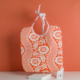 Une pochette « XCOMM_TROUSSE STYLOS OFFRANDE SAUGE » est présentée sur un présentoir blanc devant un fond orange, avec une petite carte pliée posée à proximité. la marque Toile de Jouy