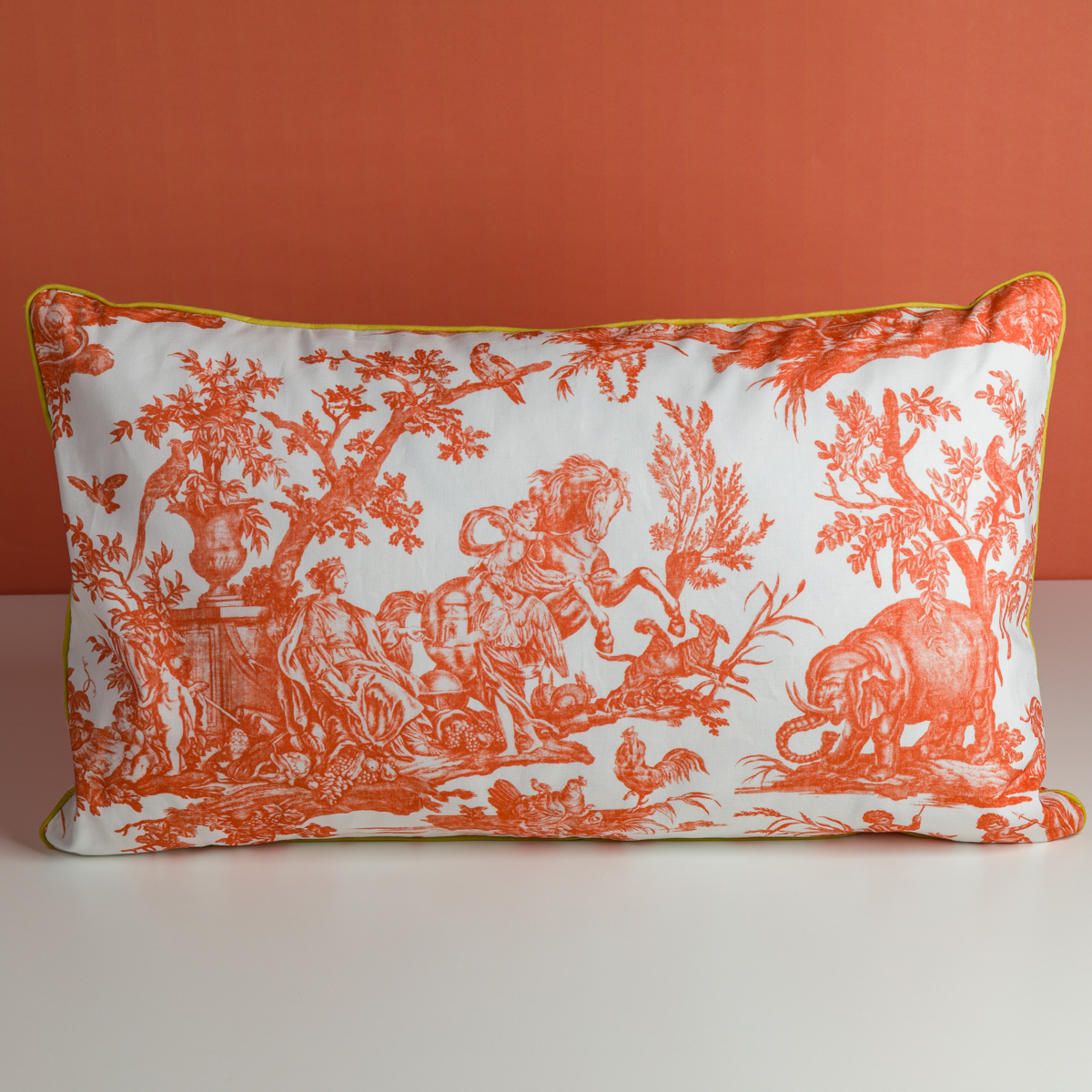 Le XCOMM_COUSSIN 30X50 FLEURS MANDARINE est un coussin rectangulaire présentant un motif de toile orange avec des personnages, des chevaux et des arbres sur fond blanc, accentué par un liseré jaune et affiché sur un fond orange. la marque Toile de Jouy