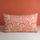 Le XCOMM_COUSSIN 30X50 FLEURS MANDARINE, un coussin rectangulaire avec un motif floral rouge et blanc composé de grandes fleurs et de rayures en forme de dentelle, repose sur une surface blanche sur un fond rouge assorti. la marque Toile de Jouy