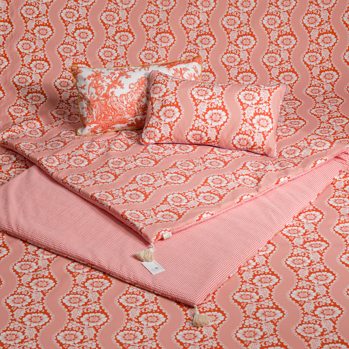 Une parure de lit avec des couettes et des oreillers à motifs roses et orange, ondulés et fleuris, surmontés de deux oreillers, dont le XCOMM_COUSSIN 30X50 FLEURS SAUGE à l'imprimé floral assorti à la parure de lit. la marque Toile de Jouy