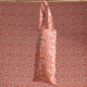 Le sac fourre-tout XCOMM_SAC ISOTHERME FLEURS MANDARINE, aux motifs floraux et ondulés orange et blancs éclatants, est suspendu à une tige en bois sur un fond à motifs assortis. la marque Toile de Jouy