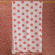 La XCOMM_SERVIETTE HAMMAM EPIS MANDARINE 100X180, une serviette blanche avec un motif floral rouge et une petite étiquette blanche, est suspendue à une tringle dorée contre un papier peint rétro ondulé à motifs floraux roses et rouges. la marque Toile de Jouy