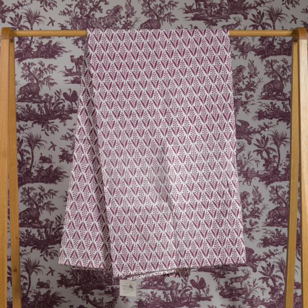 Le XCOMM_SERVIETTE HAMMAM EPIS MANDARINE 100X180, qui présente un motif marron et blanc, est suspendu à un support en bois avec un papier peint de scène pastorale marron en arrière-plan. la marque Toile de Jouy