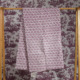 Le XCOMM_SERVIETTE HAMMAM EPIS MANDARINE 100X180, qui présente un motif marron et blanc, est suspendu à un support en bois avec un papier peint de scène pastorale marron en arrière-plan. la marque Toile de Jouy