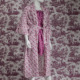 Un mannequin porte la XCOMM_NUISETTE CHARDON AMARANTE - une robe de chambre à fleurs roses et blanches - sur une tenue à motifs magenta, se fondant dans le papier peint scénique assorti pour un effet camouflé. la marque Toile de Jouy