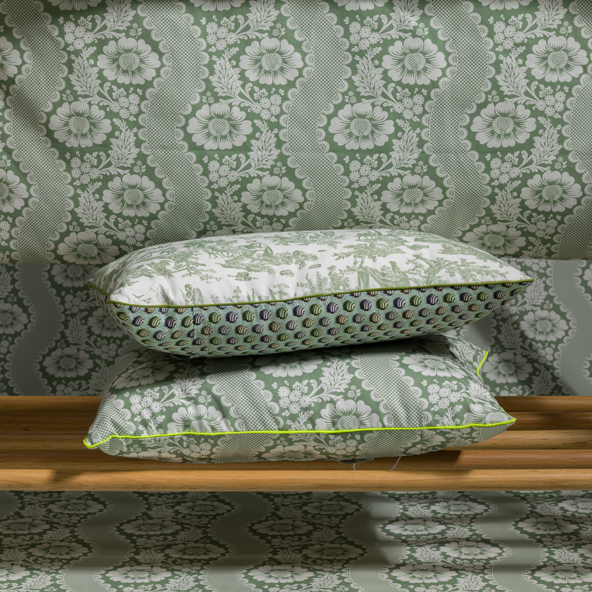 Deux coussins XCOMM_COUSSIN 30X50 FLEURS SAUGE à motifs floraux verts sont empilés sur un banc en bois, contre un papier peint floral vert et blanc assorti pour un look coordonné. la marque Toile de Jouy