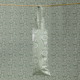 Le XCOMM_HOUSSE BOUTEILLE OFFRANDE SAUGE, avec son motif vert et blanc, est suspendu à une tringle en bois et s'intègre parfaitement dans un fond de papier peint à motifs floraux et ondulés assorti. la marque Toile de Jouy