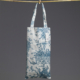 Un sac fourre-tout blanc, baptisé « XCOMM_COUSSIN 30X50 ESCARPOLETTE BLEU », orné de motifs floraux et d'oiseaux bleus très détaillés, est suspendu à une tringle horizontale par ses deux anses. Une petite étiquette blanche est fixée au sac, sur un fond gris uni. la marque Toile de Jouy