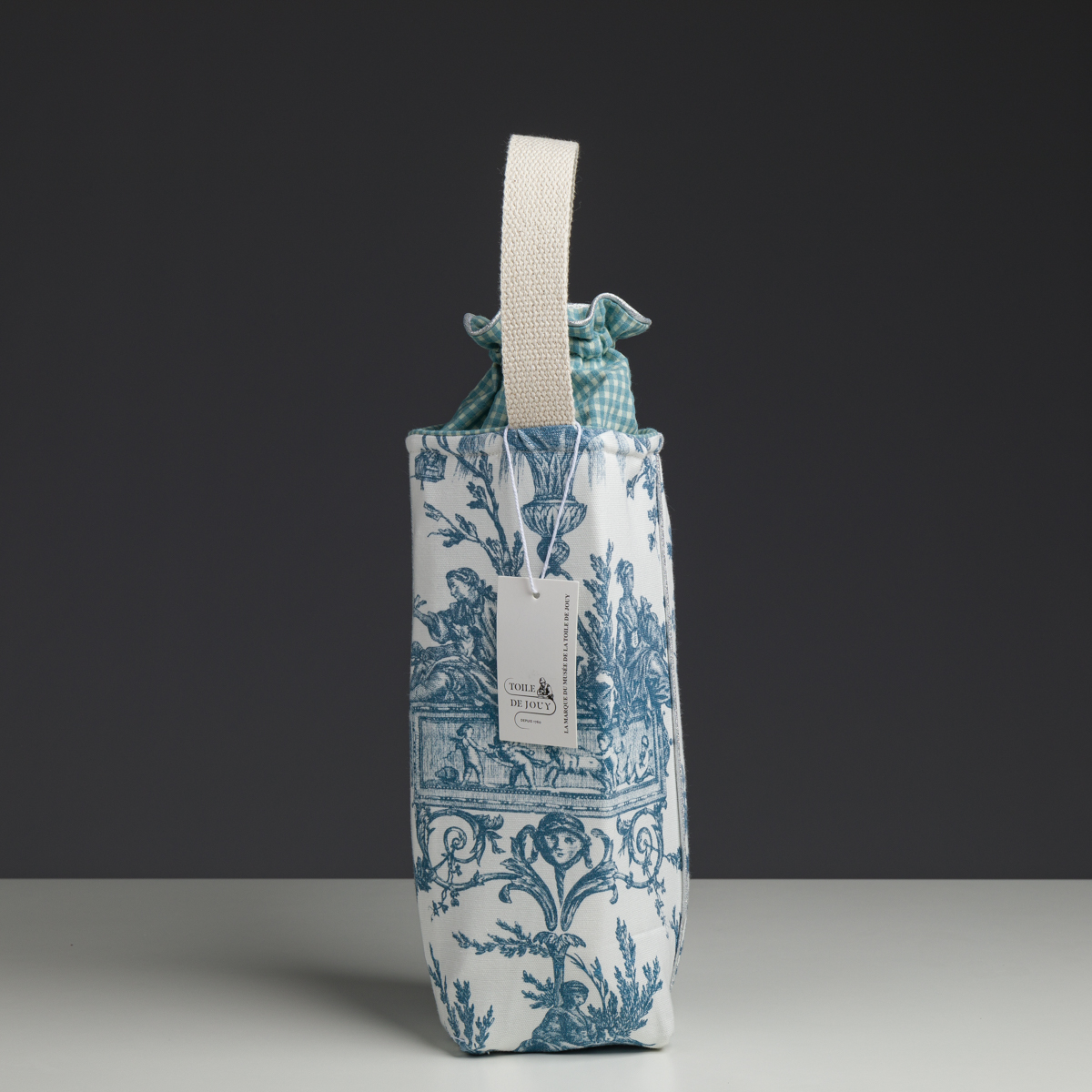 Bien sûr ! Voici une phrase réécrite en utilisant le nom du produit issu de vos données : Le XCOMM_COUSSIN 30X50 ESCARPOLETTE BLEU, composé d’un tissu à motifs bleus et blancs avec un haut à cordon de serrage à carreaux, d’une poignée de couleur crème et d’une étiquette attachée, est présenté debout sur un fond sombre. la marque Toile de Jouy