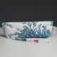 XCOMM_COUSSIN 30X50 ESCARPOLETTE BLEU, orné d'un tissu à motifs blancs et bleus et doté d'une fermeture éclair verte, se détache sur un fond sombre. À l'avant de la pochette se trouvent un stylo multicolore et une étiquette. la marque Toile de Jouy