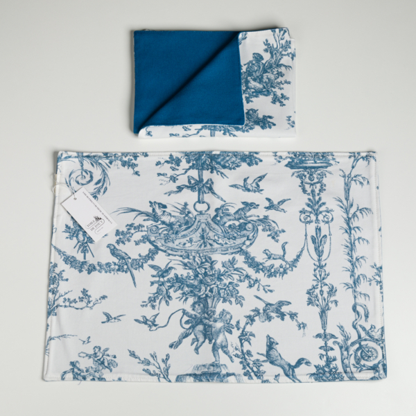 Un coussin XCOMM_COUSSIN 30X50 ESCARPOLETTE BLEU, orné d’un motif bleu et blanc représentant des oiseaux et du feuillage, accompagné d’une serviette pliée assortie présentant un côté bleu uni. Les deux articles sont disposés sur un fond blanc, l’étiquette du coussin étant visible. la marque Toile de Jouy