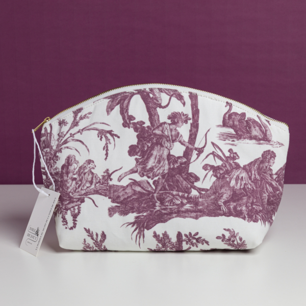 Le modèle XCOMM_TROUSSE POULETTE4 PARTIES MANDARINE est une pochette blanche à fermeture éclair, ornée d'un motif « toile » champêtre violet représentant des personnages et des animaux sur fond violet, avec une étiquette fixée à la fermeture éclair. la marque Toile de Jouy