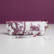 La trousse XCOMM_TROUSSE POULETTE4 PARTIES MANDARINE, une trousse blanche ornée d'un motif de cygne et d'arbres sur toile violette, est présentée sur une surface blanche, avec un stylo et une étiquette assortis placés devant, sur fond violet. la marque Toile de Jouy