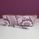 La XCOMM_TROUSSE STYLOS FLEURS AMARANTE est une pochette zippée à motif floral blanc et violet, présentée sur une surface blanche avec un stylo assorti devant, sur un fond violet uni. la marque Toile de Jouy
