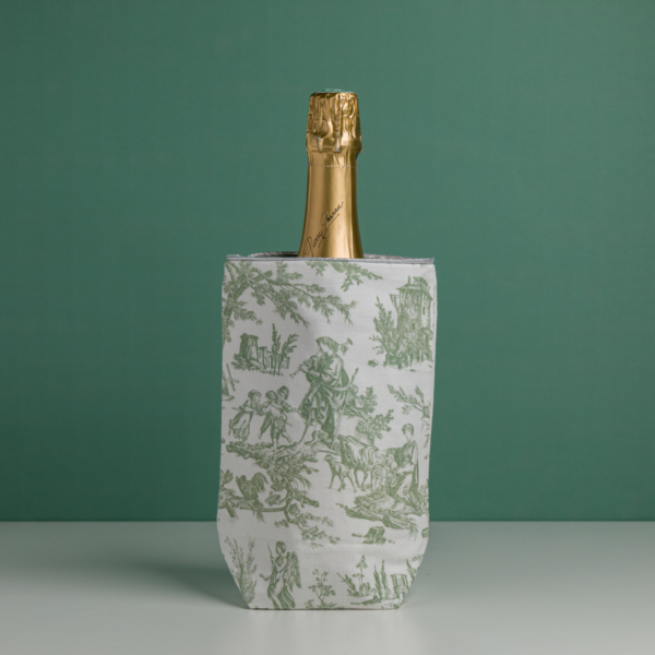 La bouteille de champagne XCOMM_HOUSSE BOUTEILLE OFFRANDE SAUGE, recouverte d'une feuille d'or, est placée dans un refroidisseur à vin décoratif à motifs blancs et verts sur fond vert uni. la marque Toile de Jouy