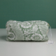 La « XCOMM_TROUSSE RECTANGULAIRE FLEUS SAUGE » est une pochette en tissu vert ornée d'un motif floral blanc, dotée d'une fermeture à glissière et d'une étiquette sur la tirette. Elle est photographiée sur une surface blanche, sur fond vert. la marque Toile de Jouy