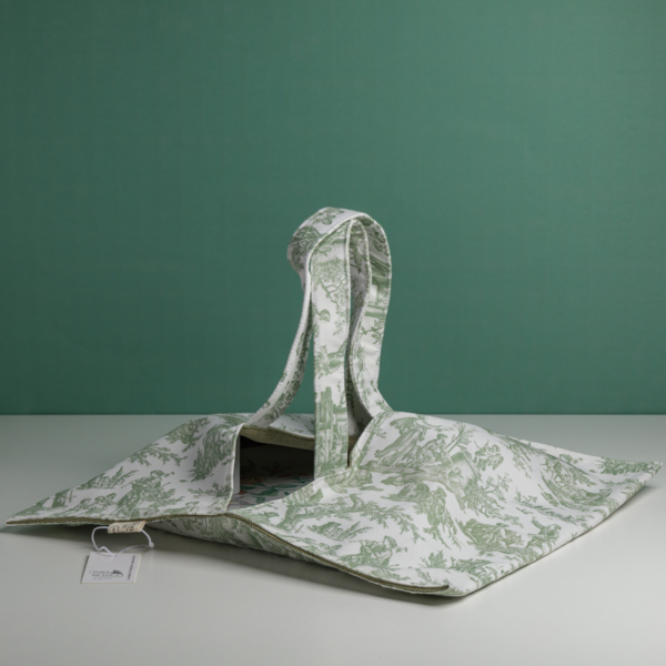Le XCOMM_SAC A PAIN OFFRANDE SAUGE, un fourre-tout en tissu souple avec des imprimés botaniques verts, deux poignées et une étiquette blanche, est présenté sur une surface blanche sur fond vert. la marque Toile de Jouy