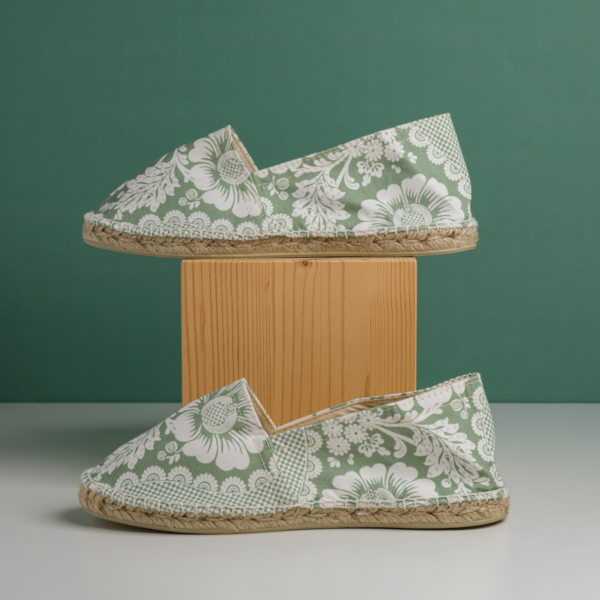 Deux espadrilles XCOMM_ESPADRILLE FLEURS MANDARINE P38 sont présentées côte à côte, l'une posée sur un bloc en bois et l'autre à même la surface, toutes deux sur fond vert. la marque Toile de Jouy