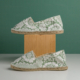 Deux espadrilles XCOMM_ESPADRILLE FLEURS MANDARINE P38 sont présentées côte à côte, l'une posée sur un bloc en bois et l'autre à même la surface, toutes deux sur fond vert. la marque Toile de Jouy