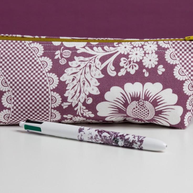 Le MATELAS DE REPOS "FLEURS STYLISÉES" MANDARINE, aux motifs floraux violets éclatants, se trouve derrière un stylo blanc aux motifs assortis, tous deux présentés sur une surface blanche propre. la marque Toile de Jouy