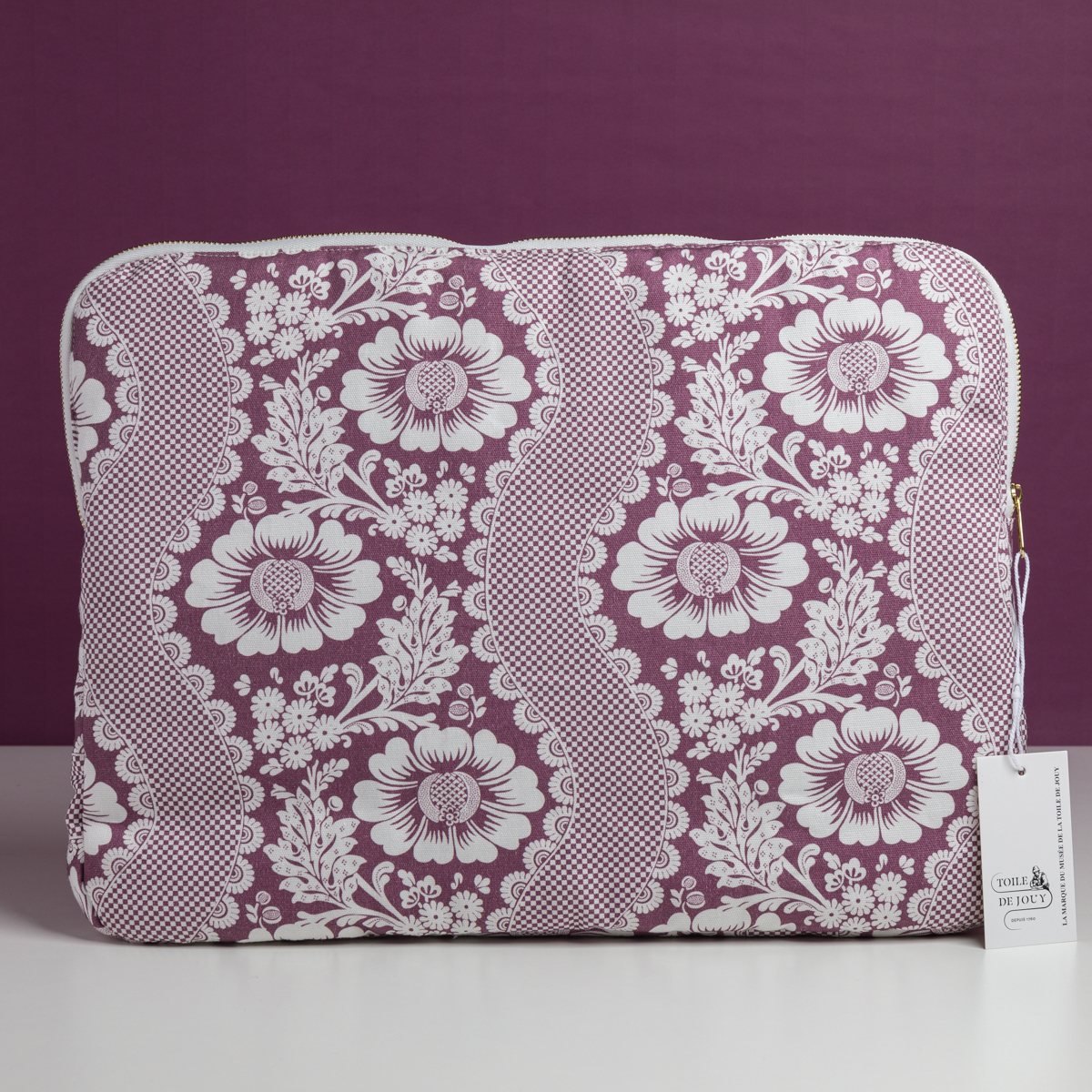 Le sac en tissu MANDARINE "FLEURS STYLISÉES" de MATELAS DE REPOS, orné d'un motif de dentelle florale violet et blanc, se tient debout sur un fond violet, avec une étiquette blanche accrochée à la fermeture éclair. la marque Toile de Jouy