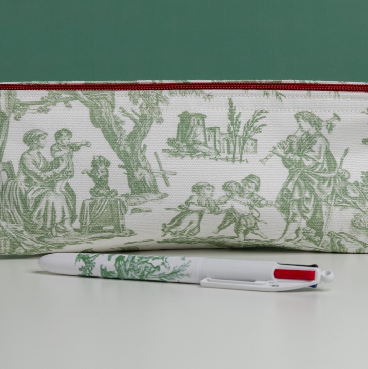 Le MATELAS DE REPOS "FLEURS STYLISéES" MANDARINE, qui présente des motifs floraux stylisés en vert sur fond blanc avec un accent rouge, est présenté avec un stylo assorti sur une surface blanche sur fond vert. la marque Toile de Jouy