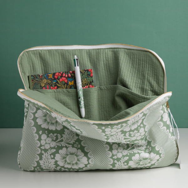 Le MATELAS DE REPOS "FLEURS STYLISéES" MANDARINE est présenté ouvert sur une surface blanche, révélant une pochette intérieure avec un stylo et une carte florale colorée, le tout sur fond vert. la marque Toile de Jouy