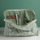 Le MATELAS DE REPOS "FLEURS STYLISéES" MANDARINE est présenté ouvert sur une surface blanche, révélant une pochette intérieure avec un stylo et une carte florale colorée, le tout sur fond vert. la marque Toile de Jouy
