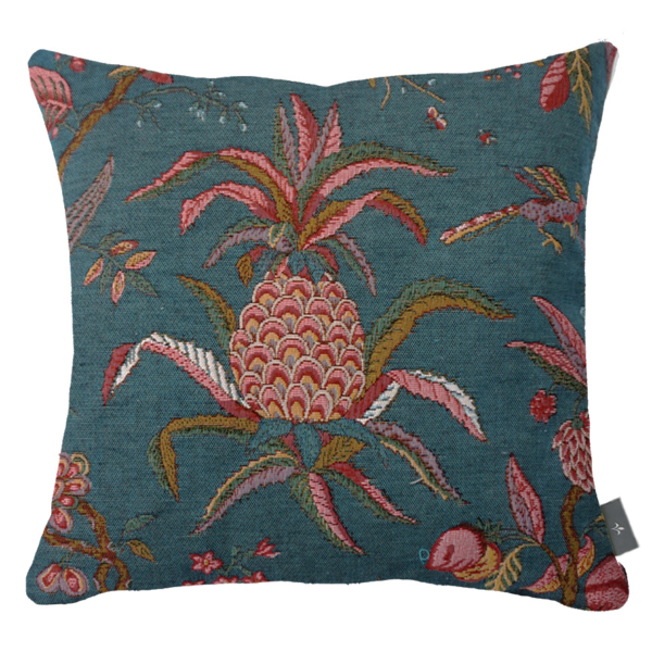 2569T Ce coussin carré, sur fond bleu sarcelle, est orné d'un motif décoratif composé de fruits et de feuilles tropicaux roses, rouges et marron, avec notamment un ananas au centre. Une petite étiquette noire est visible sur le bord droit. la marque Toile de Jouy