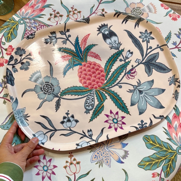 IMG_1118 Une main tient un grand plat ovale orné de motifs floraux colorés, posé sur une table recouverte d'une nappe à motifs floraux assortis, avec des verres et d'autres assiettes à motifs. la marque Toile de Jouy