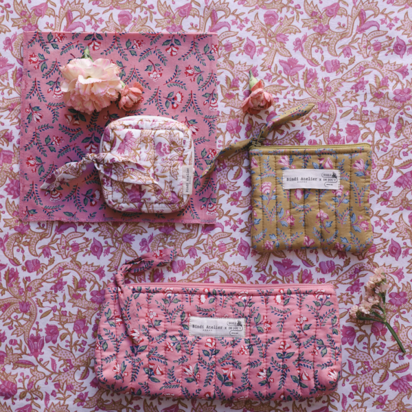 Bindi Atelier - Accessoires, sacs et foulards (71) Trois pochettes matelassées à motifs floraux issues de la collection Bindi Atelier x Toile de Jouy, présentées sur un tissu à fleurs assorti orné de petites branches de fleurs roses. la marque Toile de Jouy