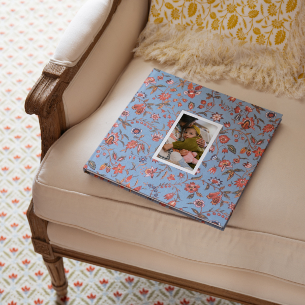 OTH_7931edited. Un album photo à motifs floraux, dont la couverture représente un enfant allongé sur un fauteuil de couleur crème. la marque Toile de Jouy